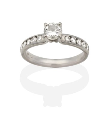 Lot 2149 - A Solitaire Diamond Ring, a round brilliant cut diamond in a claw setting, to channel set...