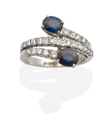 Lot 2136 - An 18 Carat Gold Sapphire and Diamond Crossover Ring, two oval cut sapphires in claw settings,...