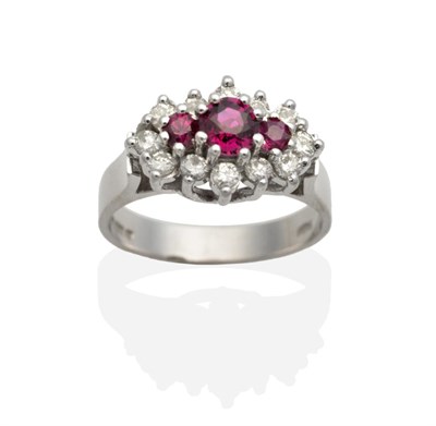 Lot 2146 - An 18 Carat White Gold Ruby and Diamond Cluster Ring, three graduated round cut rubies in claw...