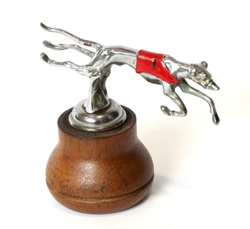 Lot 136 - A 1930s Mascot of a Greyhound Leaping Over a Fence, chrome plated wuth red race coat display...