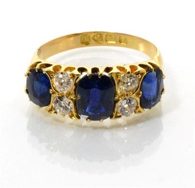 Lot 95 - An 18 carat gold sapphire and diamond ring, three oval cut sapphires spaced by pairs of old cut...