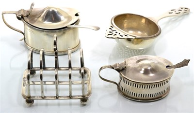 Lot 107 - Two oval silver mustard pots; a silver tea strainer, Birmingham 1931; and a small silver toastrack