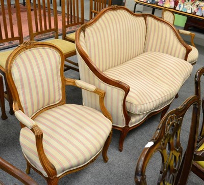 Lot 1224 - A French carved two seat sofa; and a pair of open armchairs to match, in striped upholstery (3)