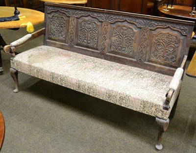 Lot 1280 - An oak settle with upholstered seat, the panelled back rest carved with thistles and roses