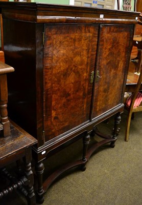 Lot 1299 - A walnut cabinet on stand, the pair of cupboard doors enclosing a shelved interior