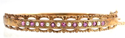 Lot 113 - A 9 carat gold Victorian revival bangle, alternating round cut rubies and seed pearls in a...