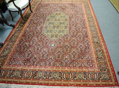 Lot 1366 - A machine made carpet of Persian design, the crimson Herati field centred by a lozenge enclosed...