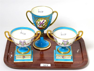 Lot 323 - A pair of Mintons parcel gilt twin handled cups on stands decorated with ribbons and laurels,...