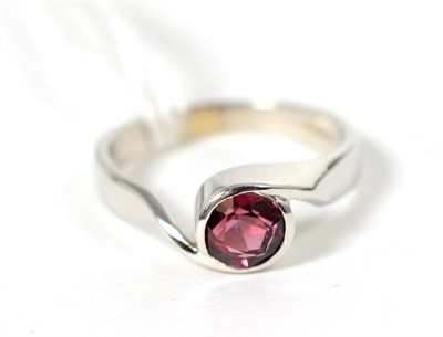 Lot 239 - An 18 carat white gold garnet ring, a round cut garnet in a rubbed over setting, to bypass...