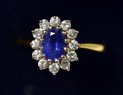 Lot 252 - An 18 carat gold sapphire and diamond cluster ring, an oval cut sapphire within a border of...