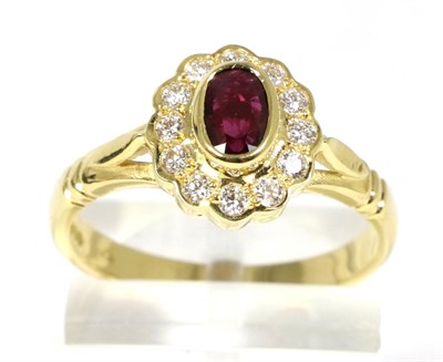 Lot 87 - An 18 carat gold ruby and diamond cluster ring, an oval cut ruby in a rubbed over setting, within a