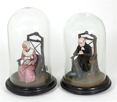 Lot 219 - A pair of novelty ceramic figures of an elderly man and woman, with nodding heads, under glass...