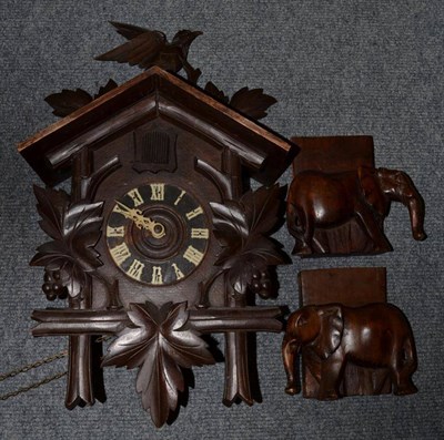 Lot 1109 - A cased cuckoo clock, with weights and pendulum; together with a pair of carved elephant...