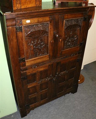 Lot 1367 - A 1920's oak four door cupboard, the two upper cupboard doors carved with monks in interior scenes