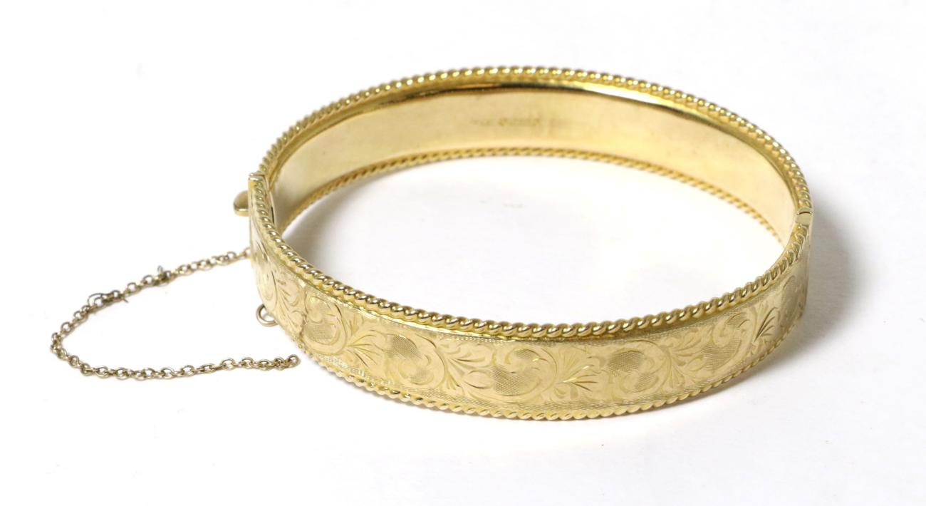Lot 24 - A 9 carat gold hinge opening bangle, with chased decoration and rope border, 6cm by 5.5cm inner...