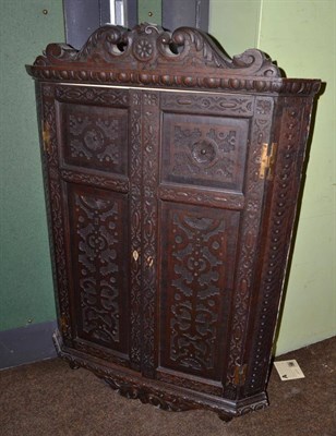 Lot 1216 - A Georgian oak corner cupboard heavily carved, twin doors, shelved interior