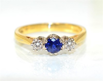 Lot 211 - An 18 carat gold sapphire and diamond three stone ring, a round cut sapphire between round...