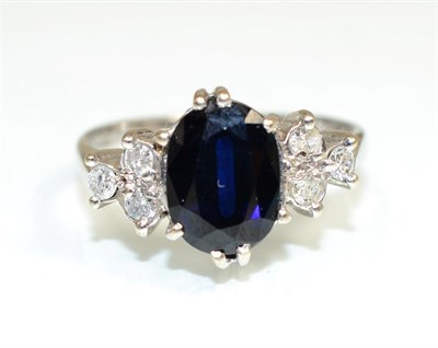 Lot 368 - An 18 carat white gold sapphire and diamond ring, an oval cut sapphire spaced by groups of...