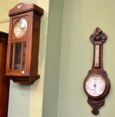 Lot 1440 - A carved oak cased aneroid barometer; and an oak wall clock, circa 1930