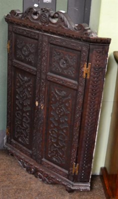 Lot 1454 - A Georgian oak corner cupboard heavily carved, twin doors, shelved interior