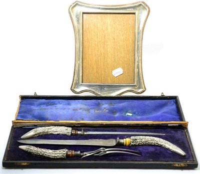 Lot 209 - A silver photograph frame together with a three piece carving set with silvered antler form handles