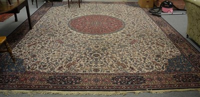 Lot 1256 - A machine made carpet of Iranian design, the ivory field of scrolling vines around a cusped...