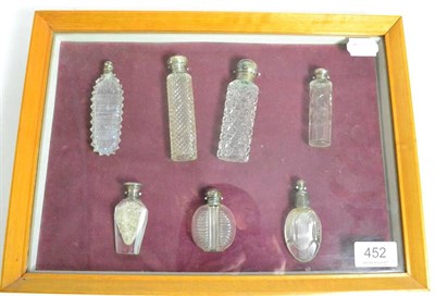 Lot 452 - A cased display of seven cut glass scent bottles, the majority with silver tops