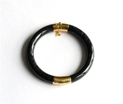 Lot 162 - A black dyed hardstone bangle with foliate engraved mounts, stamped '14K'