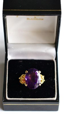 Lot 173 - An amethyst ring, an oval mixed cut amethyst in a yellow claw setting, to textured scrolling...