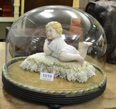 Lot 1019 - A German bisque piano baby ornament, on lace cushion, glass dome and ebonised base