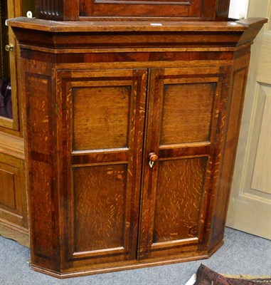 Lot 1448 - A George III cross banded paneled oak hanging corner cupboard