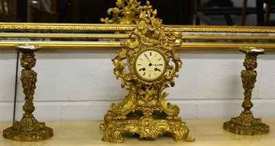 Lot 1071 - A reproduction gilt metal clock decorated with scrolls and flowers together with a pair of...