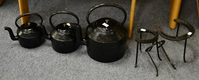 Lot 1134 - Three black painted graduated kettles on horseshoe trivets