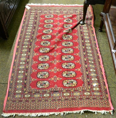 Lot 1202 - A Lahore Bukhara style rug on a red ground with two columns of quartered guls, enclosed by sunburst