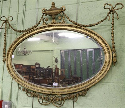 Lot 1237 - A 19th century gilt gesso oval mirror, surmounted by urns and ribbon tied swags