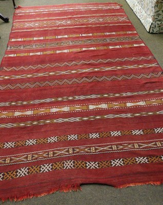 Lot 1420 - A Moroccan flat weave carpet, North West Africa, the madder field with narrow bands of...