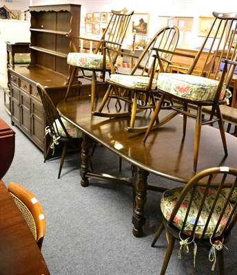 Lot 1104 - An Ercol dark elm extending dining table together with six matching stick back dining chairs...