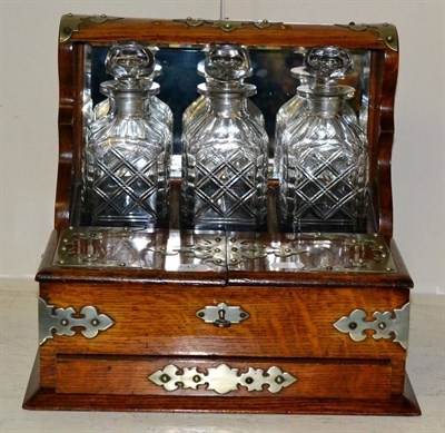 Lot 232 - An early 20th century oak three bottle tantalus, with key