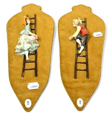 Lot 11 - A pair of Naples Capodimonte porcelain figures of girl and boy climbing ladders, on velveteen...