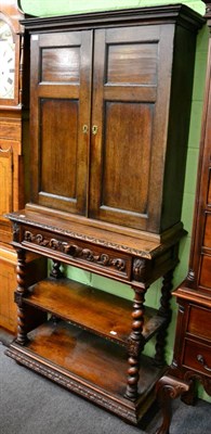 Lot 1243 - A panelled oak cupboard on stand, the stand with two tiers and fitted with a drawer