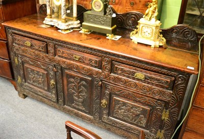 Lot 1378 - An 18th century provincial oak sideboard, the panels carved with interior scenes and flowers