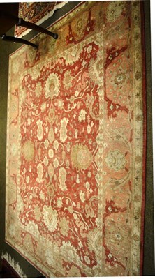 Lot 1330 - A soft brick red field rug of angular vines and palmettes enclosed by borders of palmettes...