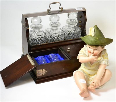 Lot 221 - A German Parian ware piano baby and a three bottle tantalus with glasses (2)