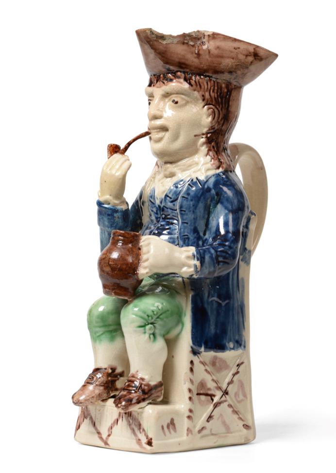 Lot 44 - A Creamware  "Thin Man " Toby Jug, circa 1780, seated wearing a manganese tricorn hat, blue...