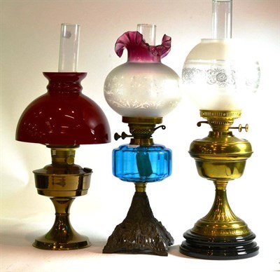 Lot 148 - An Edwardian oil lamp with blue glass font and peacock cast base and two other oil lamps (3)