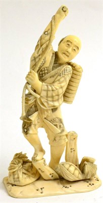 Lot 132 - A Japanese ivory Okimono, Meiji period, the figure holding a rope with baskets at his feet, losses