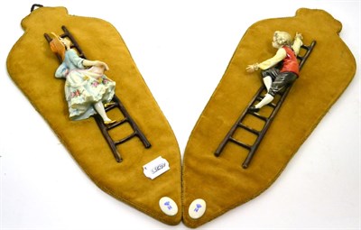 Lot 327 - A pair of Naples Capodimonte porcelain figures of girl and boy climbing ladders, on velveteen...