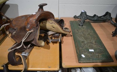 Lot 1057 - A tooled leather saddle, together with a painted cast iron stand and sign