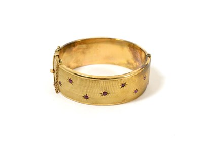 Lot 107 - A 9ct gold bangle, of textured effect, with seven round rubies inset within star motifs to the...