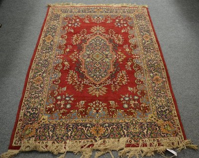 Lot 1362 - An Indian rug of Kirman design, the plain blood red field with central floral panel enclosed by...